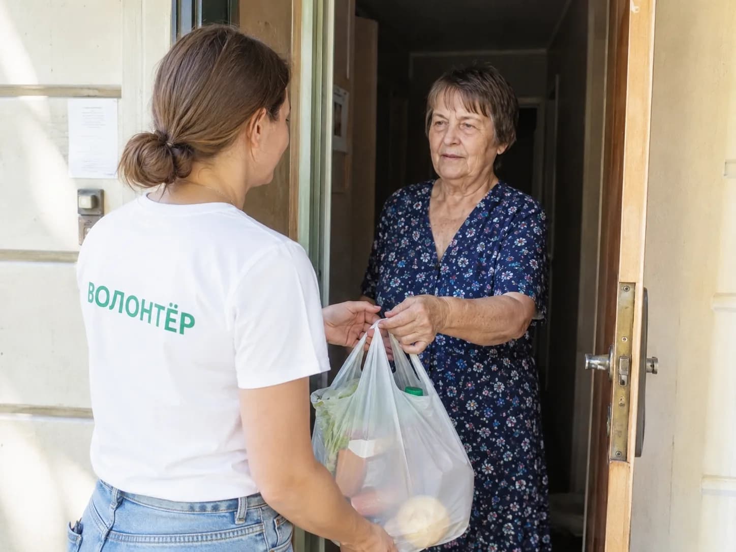 Волонтёр передаёт пакет с продуктами женщине на пороге квартиры
