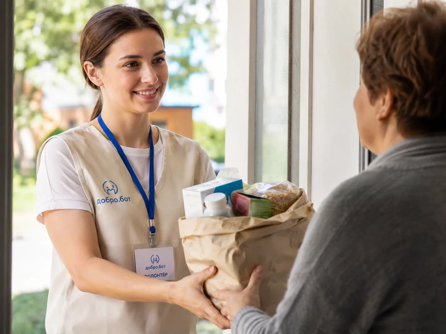 Волонтёр в жилете с бейджем передаёт пакет с продуктами и лекарствами